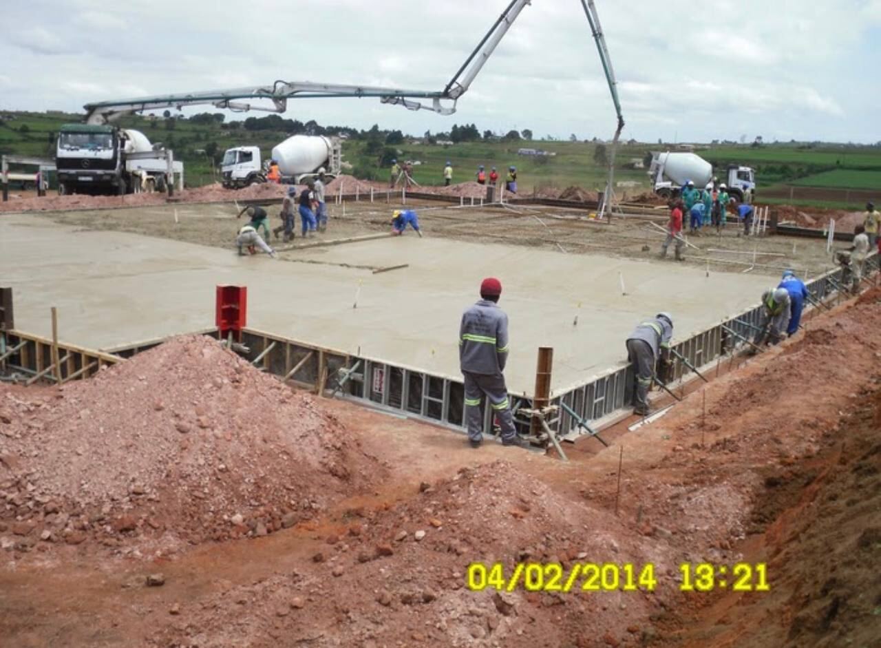 Concrete being pumped and placed across a large ground floor slab with workers finishing the surface