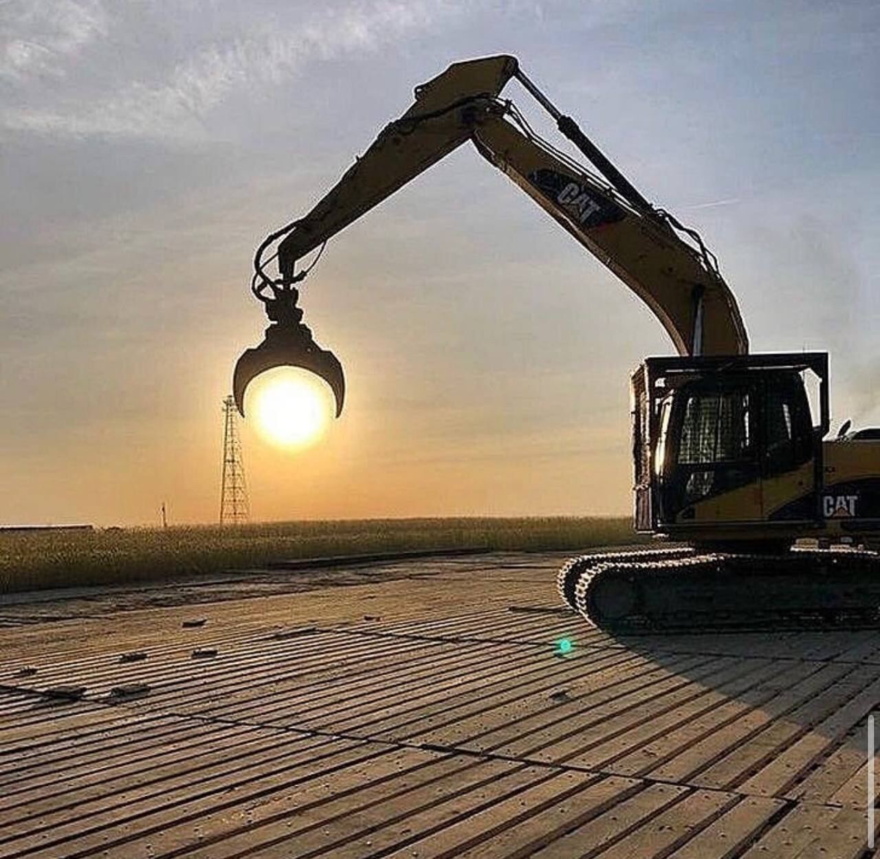 Excavator with grapple attachment silhouetted against the sunset on a Deck, Steel & Concrete site