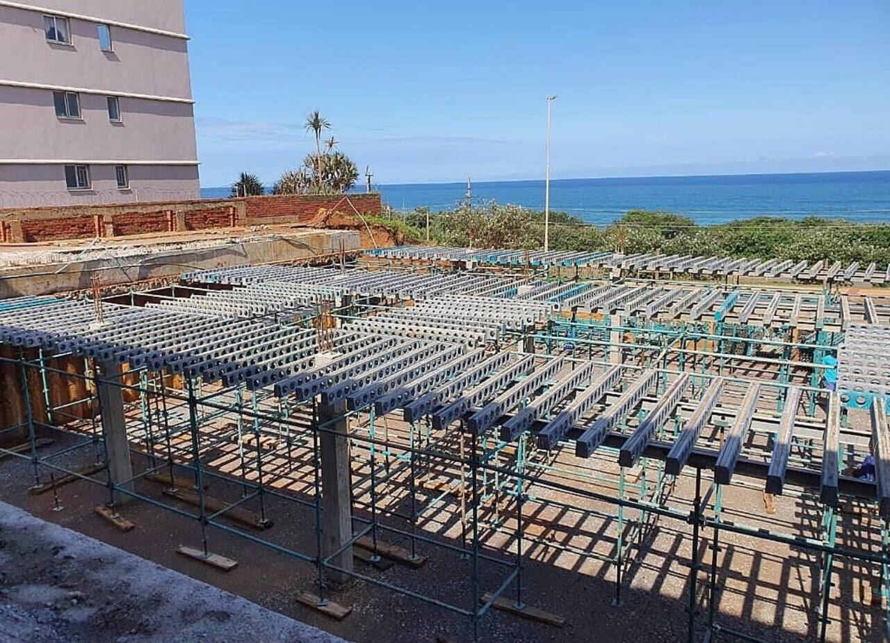 Steel formwork beams and scaffold props laid out on a coastal building site with the ocean in the background
