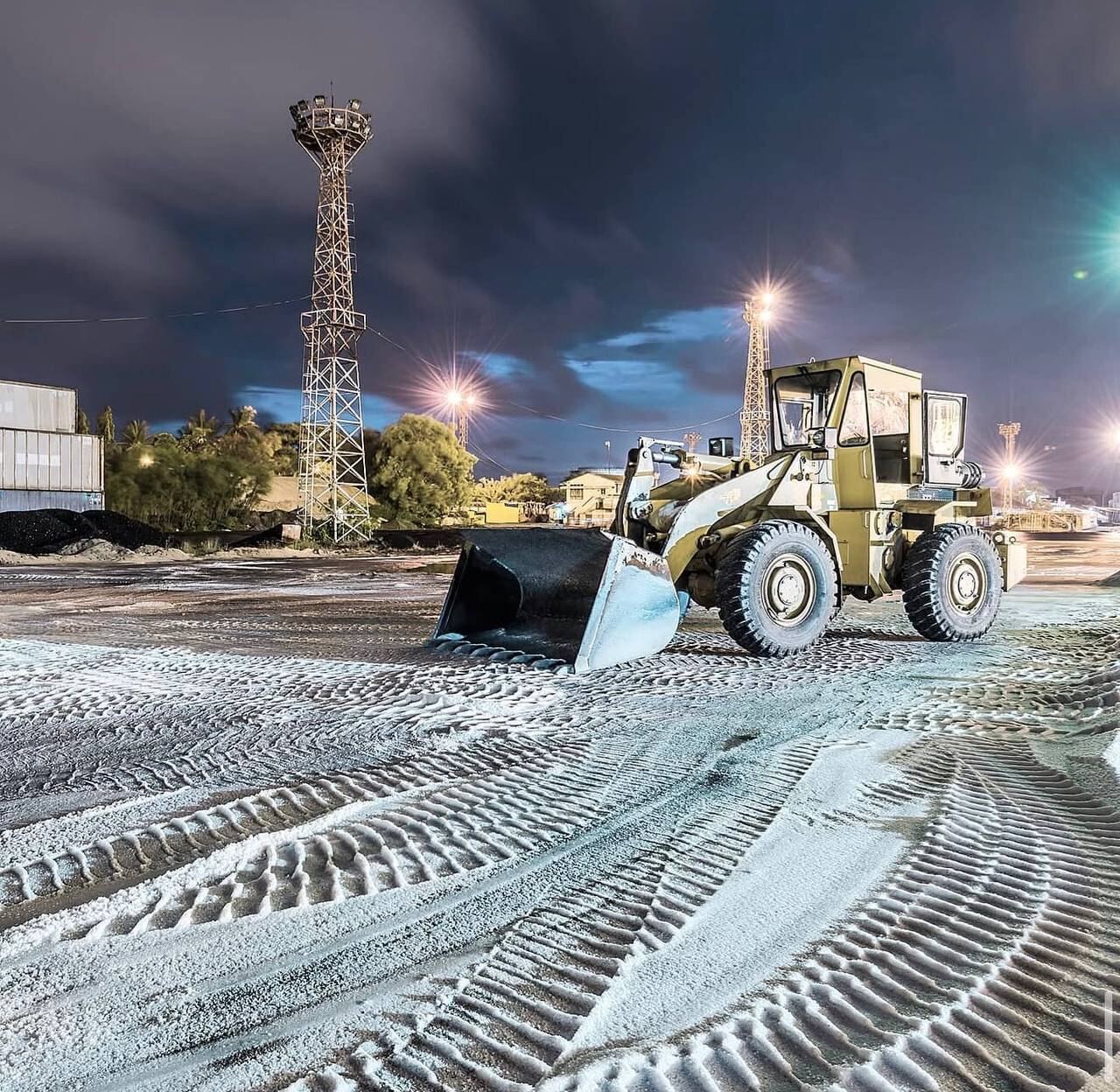 Front-end loader working at night on a frosted yard surface with floodlights