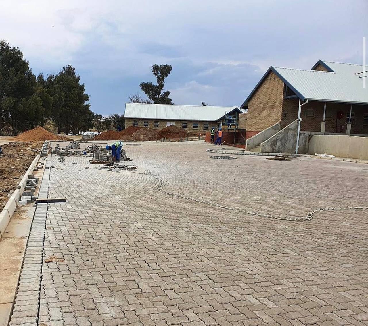 Completed interlocking concrete paving leading to brick buildings with new metal roofing on a campus site